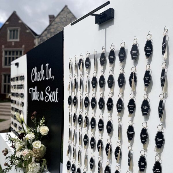 Close-up of black acrylic name tags with white lettering and tassels on a modern seating chart wall.